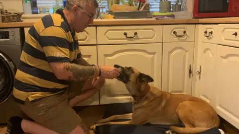 Edd Smith/BBC Man with stripy shirt taking ball from a dog's mouth