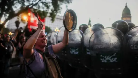 A woman bangs a lid as law enforcement officers stand guard while demonstrators protest outside the National Congress on the day of the debate on Argentina's President Javier Milei's economic reform bill, known as the "omnibus bill," in Buenos Aires, Argentina, January 31, 2024.