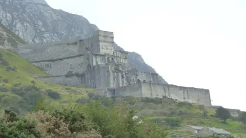 Meirion / Geograph A grey brick quarry building sits aside the mountain at Trefor, North Wales.