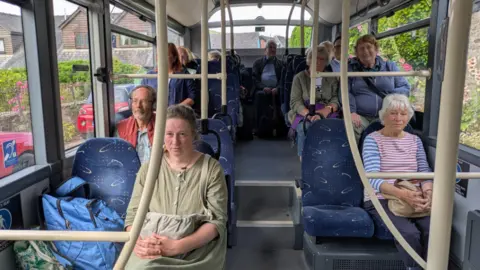 LDRS A number of people sitting on blue upholstered chairs inside a bus