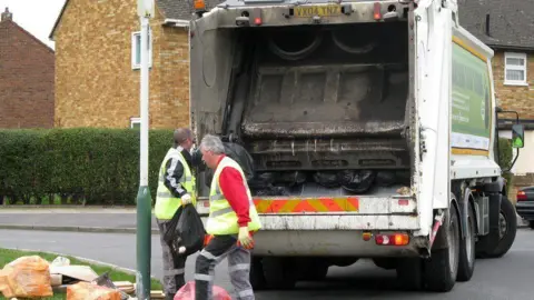 BBC Two refuse collectors standing by a bin lorry