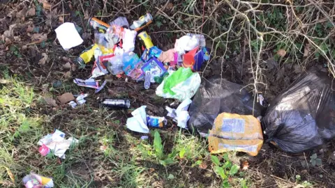 East Riding of Yorkshire Council Two black bin liners of rubbish on a grass verge, including cans, empty cartons and food bags left on the ground
