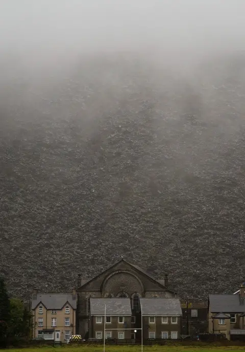 Jon Pountney A chapel and a cluster of houses with a huge slate mountain behind