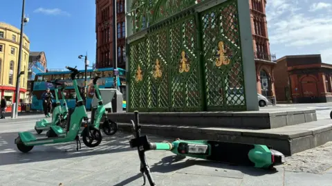 Five e-scooters on the pavement with one on its side in Liverpool city centre