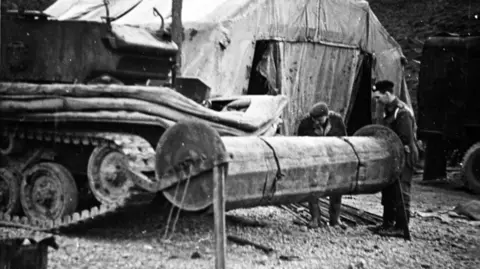 Burton upon Stather Heritage Group A black and white photograph shows two World War Two soldiers operating a large rolling machine to extend a ramp for the army tank that is also in the photograph.