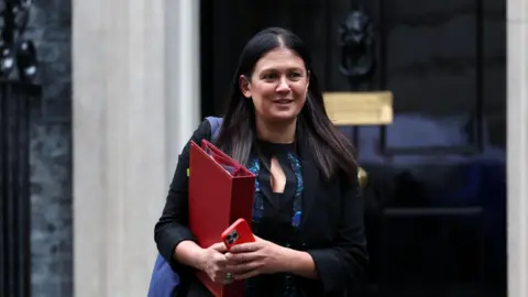 Culture Secretary and Wigan MP Lisa Nandy standing outside 10 Downing Street, holding a red binder and smartphone