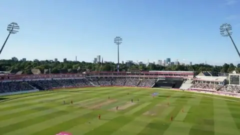 PA Media A wide shot of Edgbaston Stadium's pitch on a bright sunny day, with players involved in a match, watched from the stands by a large crowd.