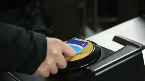 A hand tapping an Oyster card on a Tube entrance barrier.