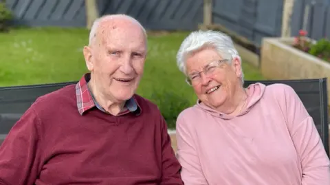 Alison Douglas Ken Jack in red jumper and checked shirt, with Eleanor Jack wearing glasses with a pink top