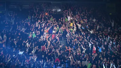 Getty Images A wrestler is walking down steps as a crowd of people surround him and reach towards him. 