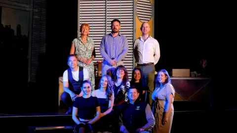 Grand Theatre Wolverhampton Theatre staff and City of Wolverhampton College staff with performing arts students. There are 10 people in the picture and they look like they are on a stage. 