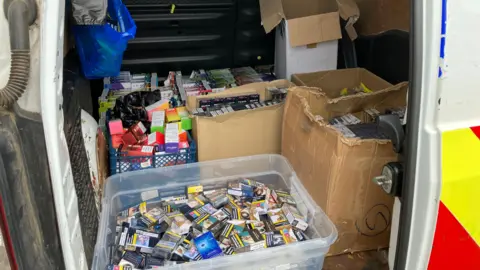 Central Bedfordshire Council Boxes of illegal vapes, tobacco and cigarettes in a number of boxed in the back of a van. There are white plastic boxes and cardboard boxes. 