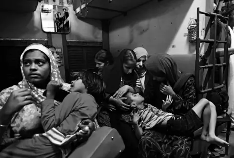 Madhuraj/Kochi Biennale Foundation Mother sit holding their babies on their laps. Some of the children have visible deformities and look weak.