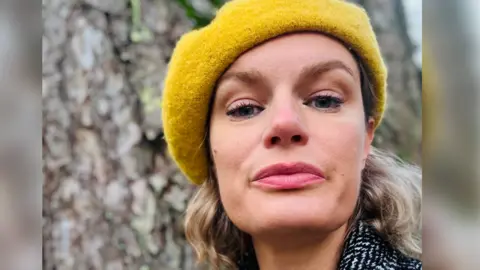 Tracy Harris Head shot of Tracy Harris wearing a yellow beret, standing in front of a tree.