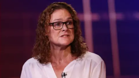 Getty A woman with curly hair and glasses wearing a white top speaking 