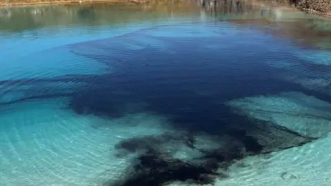 PA Media A large turquoise body of pater with black dye in.