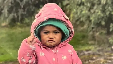 Tavia Da Costa wearing a pink coat with flowers on it and a green hat underneath. 