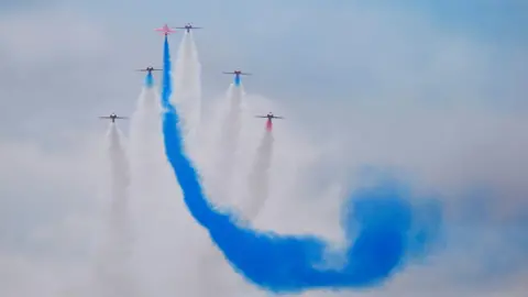 PA Media Planes are seen in the sky with colourful condensation trails left behind in the sky. The main colour is blue, others are white.