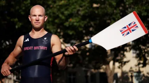 Getty Images Sam Murray in his Great Britain rowing gear holding a white ore with a Union Jack on it