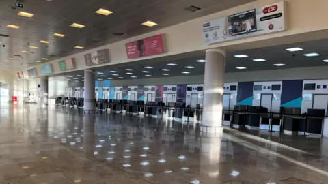 BBC/Tom Ingall An empty row of airport check in desks.