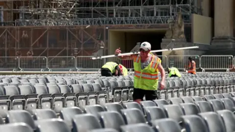 Labourers working outdoors setting up a stage and seats