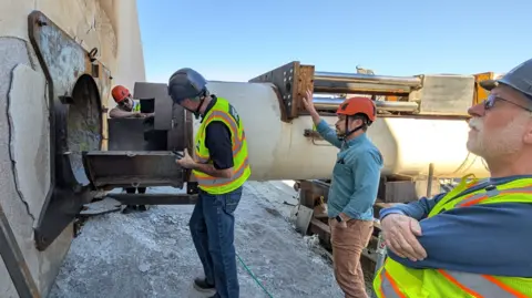 Earthgrid Four engineers stand close to a large metal cylinder which containers the Earthgrid boring machine. 