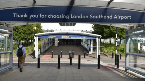 Getty Images Entrance to Southend Airport from car park showing a man wearing a rucksack walking towards a covered walkway with a sign saying 'Thankyou for choosing London Southend Airport'