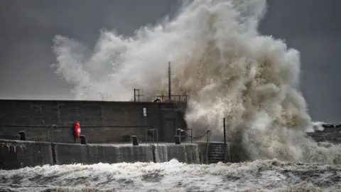 Chris Reekie Waves crashing over a harbour wall in St Andrews under a dark sky.