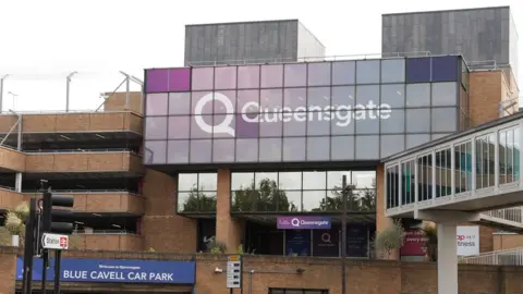 Martin Giles/BBC A multi-storey building and car park, which has the purple branding and white lettering reading QUEENSGATE. It is a cloudy day. There is a sign for the BLUE CAVELL CAR PARK.