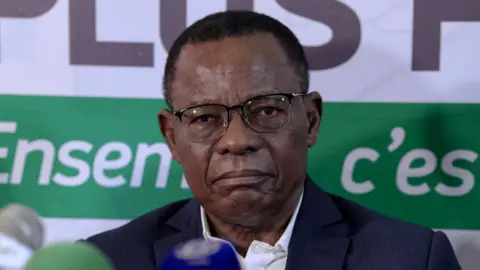 A close-up shot of Maurice Kamto. He has short hair and glasses and is wearing a blue jacket.