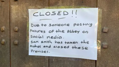A photo of a sign stuck outside the Abbey pub in Darley Abbey, reading: "Closed due to someone posting pictures of the Abbey on social media. Sam Smith has taken the alcohol and closed these premises."