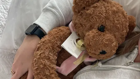 Jade Morris A teddy bear with a gold coloured bow around its neck. There is also a larger light pink bow beneath the golden one.
