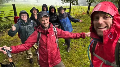 Jamie Rudd Jamie Rudd surrounded by six people all in wet-weather gear in a field and putting their thumbs up