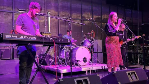 Supplied Kaitlin Robson is performing on stage with a band. She is singing, while others play a keyboard, guitar and the drums.