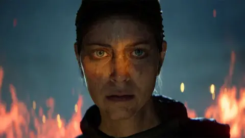 A computer-generated but extremely lifelike image of a female character. Her face looks battle-marked, possibly blood-spattered and flames rage in the background behind her. Her expression is stoic.