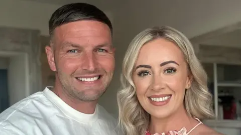 Michael Harkin Michael Harkin has short brown hair. He is smiling and wearing a white T-shirt. Claire Harkin is standing beside him. She has long blonde hair and is wearing a floral dress.