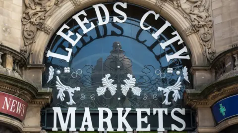 Leeds City Council Leeds City Markets sign which is large white lettering and some foliage, set in a stone archway over the door to the market