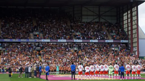 PA Media Teams and staff join a minute's silence for victims of the Bradford City fire before the Sky Bet League Two match at the University of Bradford Stadium.