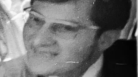 Black and white close up photo of Robert Price wearing spectacles, looking leftwards.