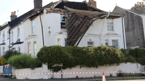 A roof collapsing off a large white property.