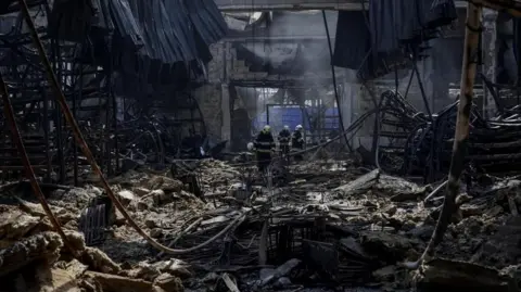 路透社 消防员在昨天遭俄罗斯空袭的购物中心现场工作