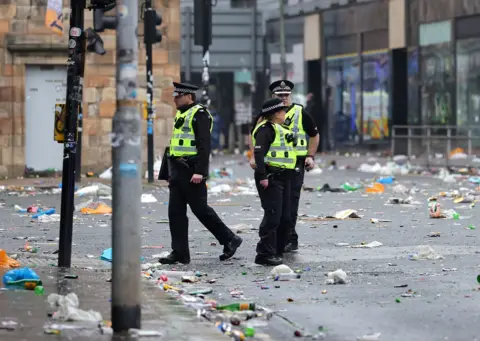 PA Media Police Scotland officers walk along a city street covered in litter and debris following large crowds gathering in Glasgow.
