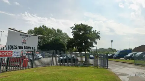 Google Sign which reads Ilkeston Town Football Club in front of a car park