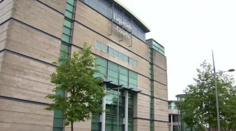 BBC An exterior shot of Laganside Courts in Belfast. A large grey brick building with a number of windows and large doorway. Two large trees can be seen near the entrance.