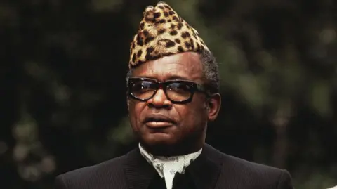 Getty Images Voormalig president van de Democratische Republiek Congo Mobutu Sese Seko met een hoed van luipaardhuid, een bril en een donker pak en das