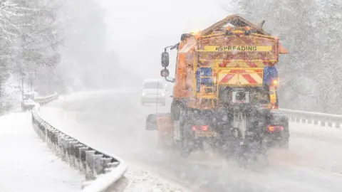 Paul Campbell/PA Wire A generic photograph of a yellow gritter lorry driving along a main road