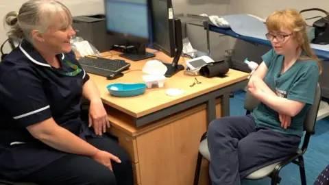 A nurse, a young patient, and her mother, all sitting in a medical office.
