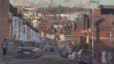 Peter Brown An oil painting of a residential street in Bristol. The road is steep and there are cars parked on either side of the road. The street is lined with houses. In the distance there are colourful houses. A person can be seen walking down the street.