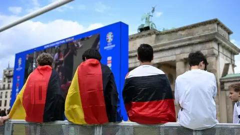     RALF HIRSCHBERGER/AFP Deutschland-Fans warten im öffentlichen Fußball-Zuschauerbereich vor dem Wahrzeichen des Brandenburger Tors vor dem Viertelfinalspiel der UEFA Euro 2024 zwischen Spanien und Deutschland am 5. Juli 2024 in Berlin, Deutschland.