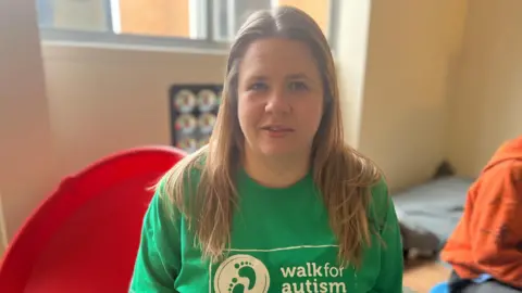 Woman with long blonde hair and green t shirt sat on a stool in a small play area room